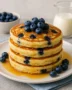 Stack of fluffy blueberry buttermilk pancakes topped with fresh blueberries and maple syrup