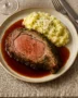 Slow-roasted herb-crusted prime rib sliced with red wine jus and creamy truffle parmesan mashed potatoes on a white serving platter